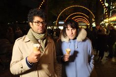 two people eating ice cream at night on the street with christmas lights in the background