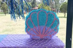 a purple and blue chair with a pink shell on it's back sitting under a tree