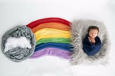 a baby wrapped in a rainbow blanket next to a pile of blankets on a white background