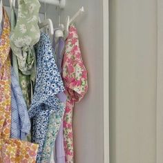 several different colored shirts hanging from hooks on a wall next to an open closet door