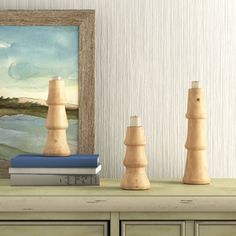 three wooden candlesticks sitting on top of a dresser next to a painting and books