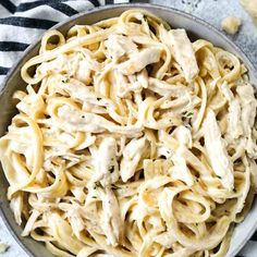 a bowl filled with chicken alfredo pasta on top of a striped table cloth and black and white napkin