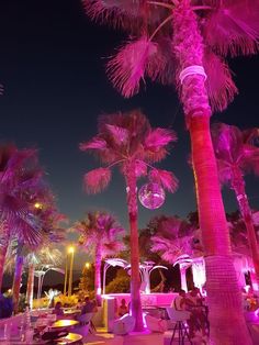 palm trees lit up at night with people sitting under them and tables in the foreground