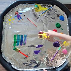 a child is playing with plastic spoons and toothbrushes on tin foil