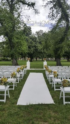 an outdoor ceremony setup with white chairs and yellow flowers on the aisle, surrounded by trees