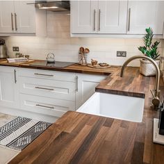 a kitchen with white cabinets and wood counter tops, an island sink and dishwasher