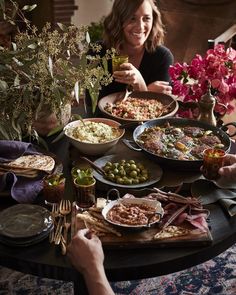 a woman sitting at a table filled with plates of food and flowers in front of her