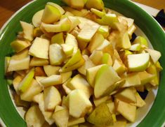 a green bowl filled with sliced apples on top of a table