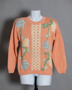 an orange sweater with flowers on it sitting on a mannequin's head