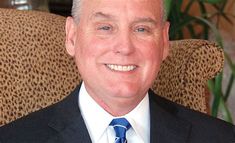 a man in a suit and tie smiling at the camera while sitting on a chair