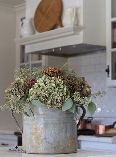 a metal bucket filled with plants on top of a kitchen counter next to an oven