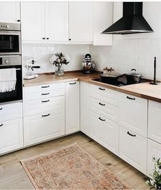 a kitchen with white cabinets and wooden counter tops, an area rug on the floor