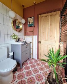 a bathroom with a toilet, sink and potted plant on the tiled flooring