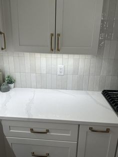 a kitchen with white cabinets and marble counter tops, gold pulls on the cupboards