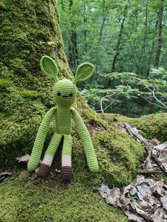 a green stuffed animal sitting next to a moss covered tree