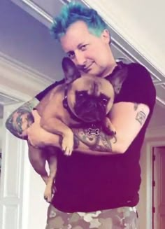 a man with blue hair holding a small pug in his arms and smiling at the camera