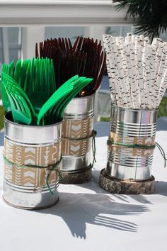 two tin cans with green and brown flowers in them on a table outside, one has grass sticking out of it