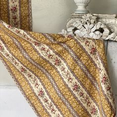 a bed covered in a yellow and brown blanket next to a white headboard with a mirror on top of it