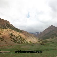 the mountains are covered in green grass and brown dirt, with white clouds above them