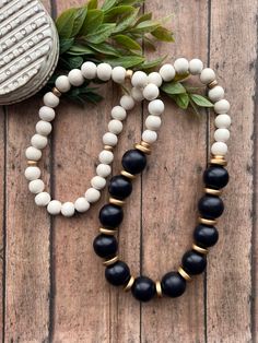 two black and white beaded necklaces sitting on top of a wooden table next to a potted plant