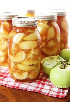 four jars filled with apple slices sitting on top of a table next to an apple