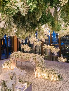 an elegant wedding setup with white flowers and greenery hanging from the ceiling, surrounded by candles