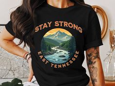 Stay Strong - East Tennessee Strong T-Shirt - Proceeds for Flood Relief Show your support for the resilient communities of East Tennessee with this beautifully designed "Stay Strong" T-shirt. Featuring a powerful, heartwarming illustration of the Appalachian Mountains and flowing rivers, this T-shirt symbolizes the strength, unity, and hope of the people affected by the recent floods in towns such as Erwin, Unicoi, Greeneville, and surrounding areas. 100% of the profits from this T-shirt will go directly to help families who have been devastated by the floodwaters, providing aid and relief as they rebuild their homes and lives. Key Features: Design: "Stay Strong - Erwin, Tennessee" graphic showcasing the natural beauty of the Appalachians with bold, modern typography. Material: Super soft Erwin Tennessee, Inspirational Graphic Tees, Western North Carolina, East Tennessee, Stay Strong, The Hamptons, Tennessee, North Carolina, Graphic Tees