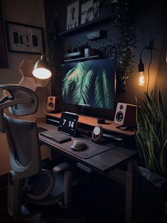 a computer desk with a monitor, keyboard and speakers on it in front of a potted plant