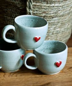 three white cups with red hearts on them sitting next to a basket filled with straw