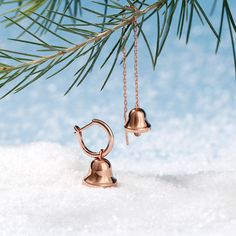 two bells hanging from a tree branch in the snow, one is gold and the other is silver