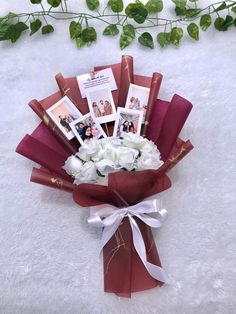 a bouquet of white roses wrapped in red paper and tied with ribbon on a white surface