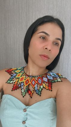 a woman with black hair wearing a blue dress and colorful beaded neck piece, posing for the camera