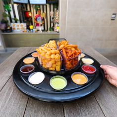 a black plate topped with fries and dipping sauces on top of a wooden table