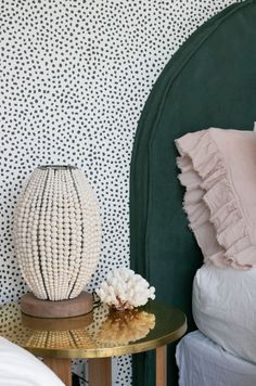 a green headboard next to a small table with a white flower on it and a gold side table