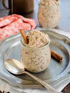 two jars filled with oatmeal sitting on top of a silver plate next to spoons