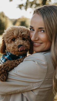 a woman holding a dog in her arms and smiling at the camera while she holds it up to her chest