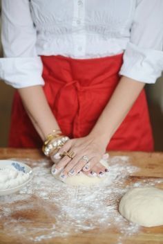 a woman in an apron is kneading dough on a wooden table with other ingredients