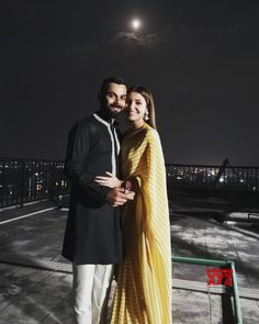 a man and woman standing next to each other in front of the moon at night