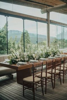 a long table set up with flowers and place settings in front of large glass windows