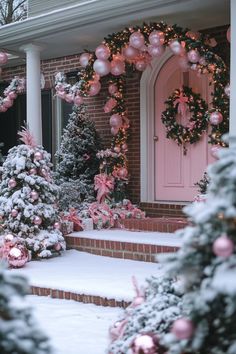 christmas trees and wreaths are on the front steps of a house with pink doors