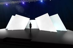 a man is standing in front of three white cubes on a stage with bright lights