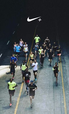 a group of people running down a street at night with a white nike logo above them