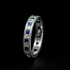 a white gold ring with blue sapphires and diamonds on the side, against a black background