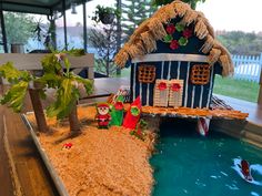 a small house made out of sand next to a pool with plants and decorations on it