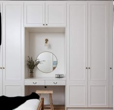 a bedroom with white cupboards, mirror and stool