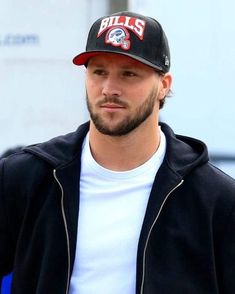 a man with a baseball cap on is looking at the camera while wearing a black jacket and white t - shirt