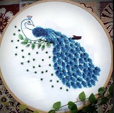 a blue embroidered peacock with green leaves on it