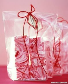 three pink soap bars wrapped in cellophane and tied with red twine on a pink surface