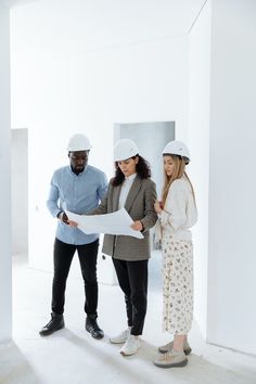 three people in hardhats looking at blueprint on the floor with one person holding a large piece of paper