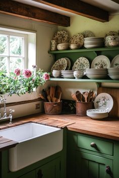 a kitchen with green cabinets and white dishes on the shelf above the sink is filled with flowers